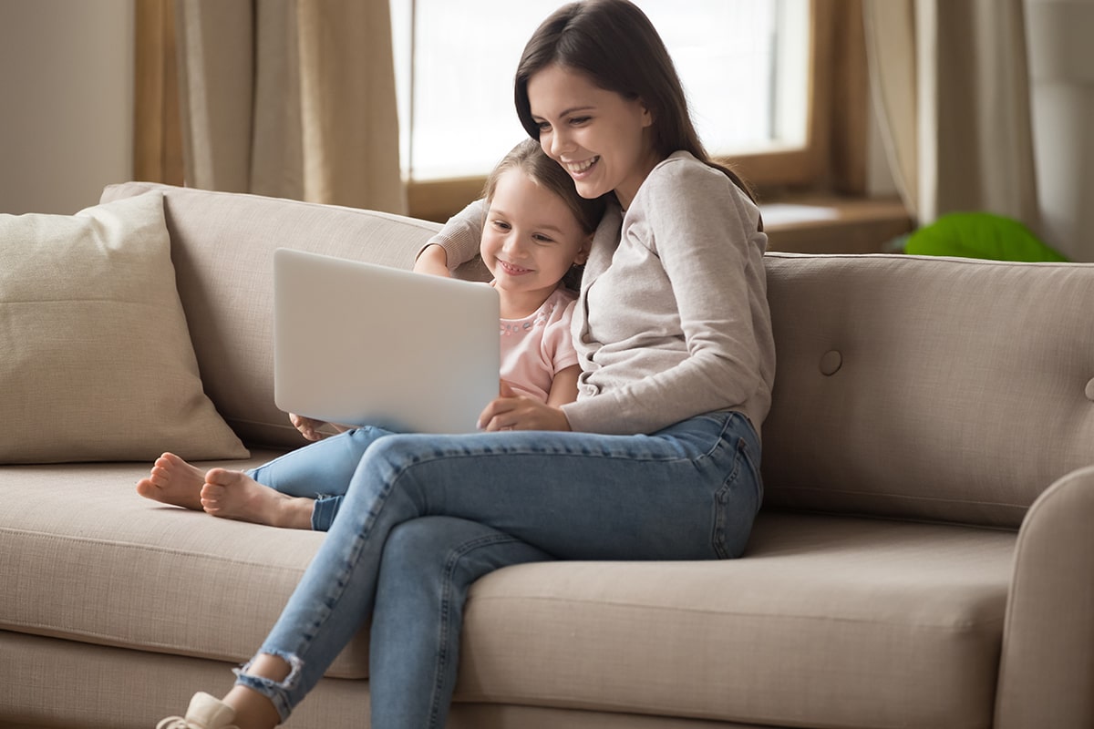 Mom sitting on couch with her daughter looking at a laptop.